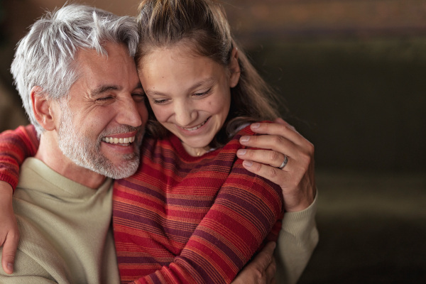 A portrait of teenage daughter hugging her happy father at home.