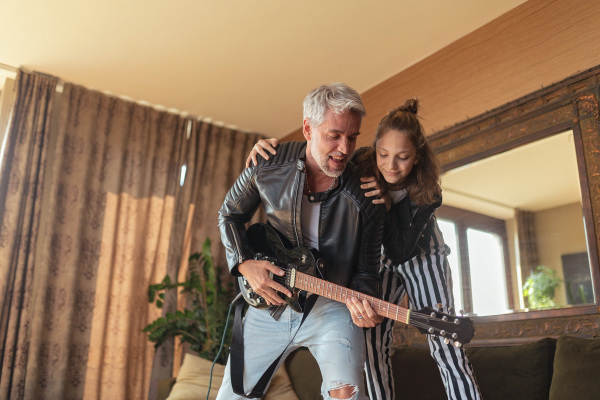 A father rock guitarist having fun and and dancing with his teenage daughter at home.