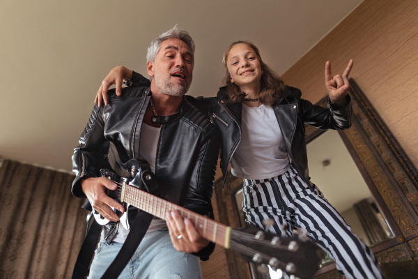 A father rock guitarist having fun and and dancing with his teenage daughter at home.