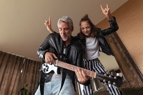 A father rock guitarist having fun and and dancing with his teenage daughter at home.