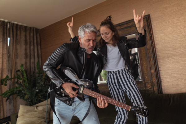 A father rock guitarist having fun and and dancing with his teenage daughter at home.