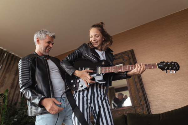 A father rock guitarist having fun and and dancing with his teenage daughter at home.