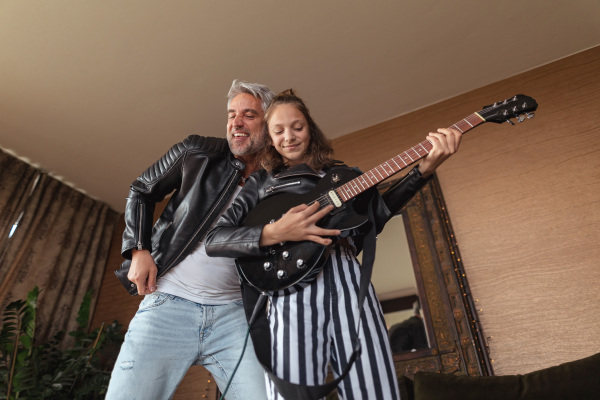 A father rock guitarist having fun and and dancing with his teenage daughter at home.