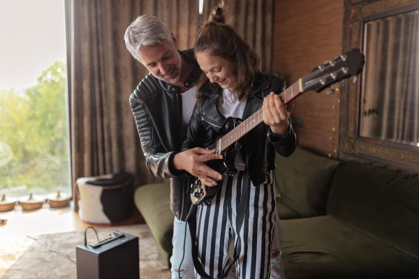 Father rock guitarist learning his teenage daughter to play electric guitar at home.