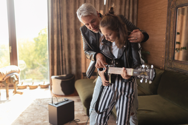 Father rock guitarist learning his teenage daughter to play electric guitar at home.