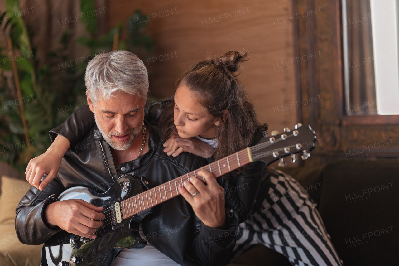 Father rock guitarist learning his teenage daughter to play electric guitar at home.