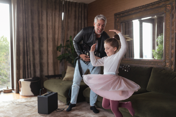 A father rock guitarist having fun and dancing with his little daughter at home.