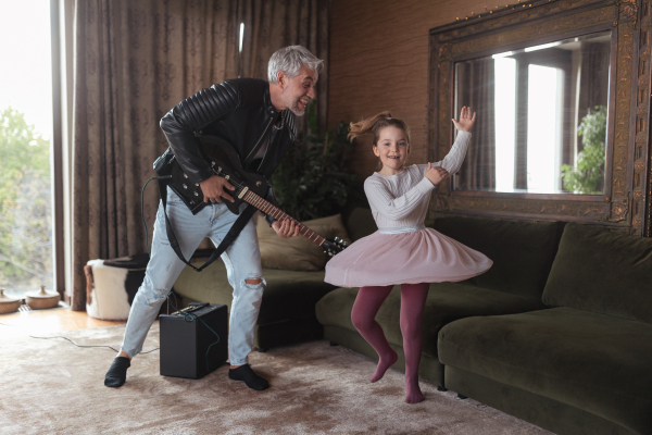 A father rock guitarist having fun and dancing with his little daughter at home.