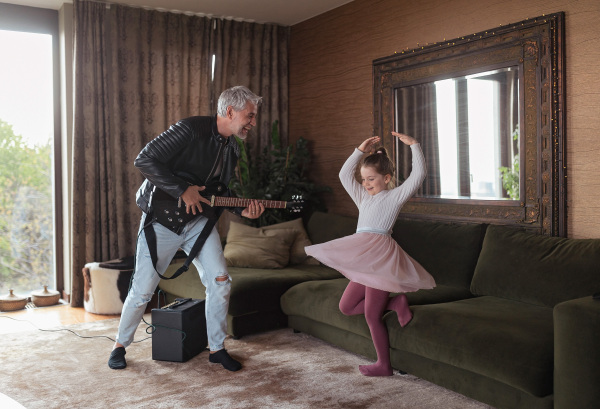 A father rock guitarist having fun and and dancing with his little daughter at home.