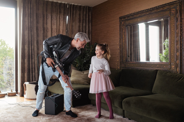 A father rock guitarist having fun and and dancing with his little daughter at home.