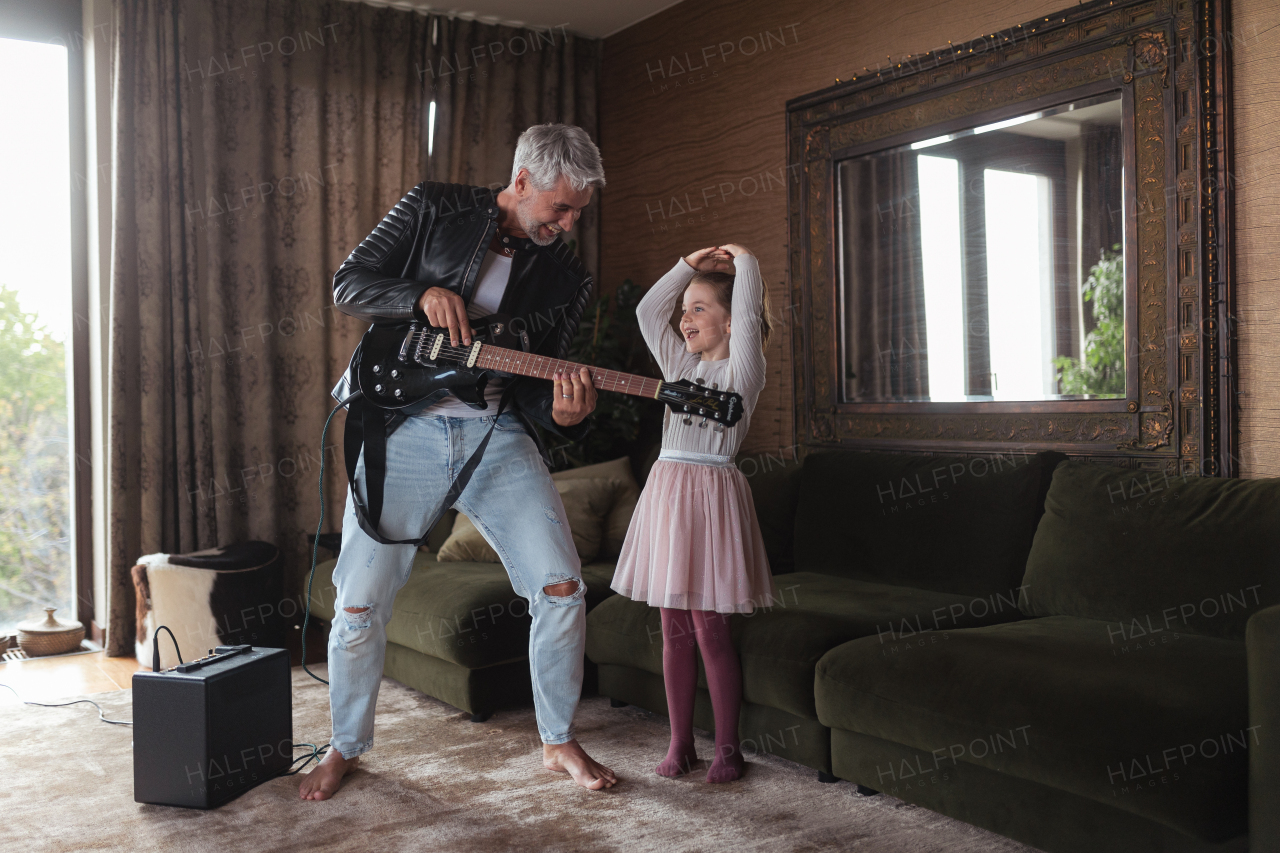 A father rock guitarist having fun and dancing with his little daughter at home.