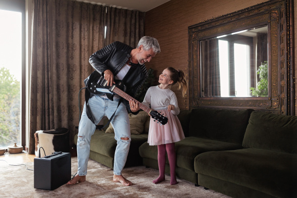 A father rock guitarist having fun and dancing with his little daughter at home.