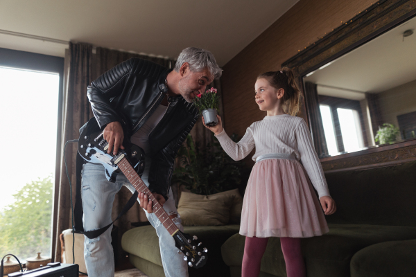 A father rock guitarist having fun and dancing with his little daughter at home.