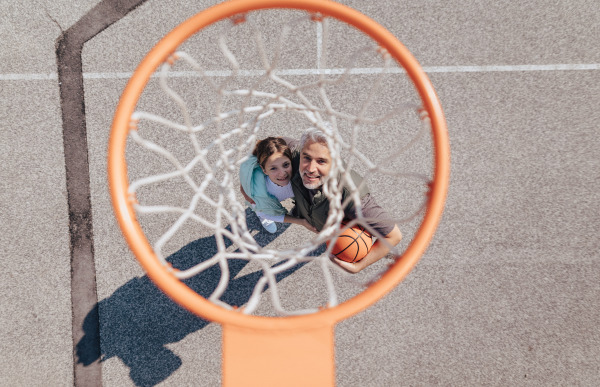 A happy father and teen daughter embracing and standing under a basketball hoop net, directly above