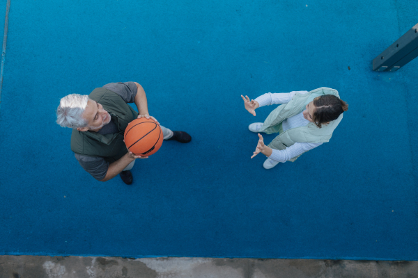 A father and teenage daughter playing basketball outside at court, high angle view.