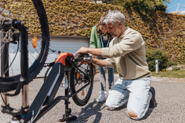 A happy father with teenage daughter repairing bicycle in street.