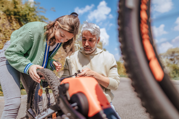 A happy father with teenage daughter repairing bicycle in street in town.