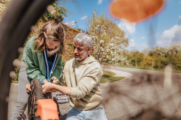 A happy father with teenage daughter repairing bicycle in street in town.