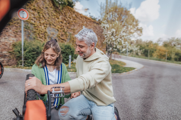 A happy father with teenage daughter repairing bicycle in street in town.