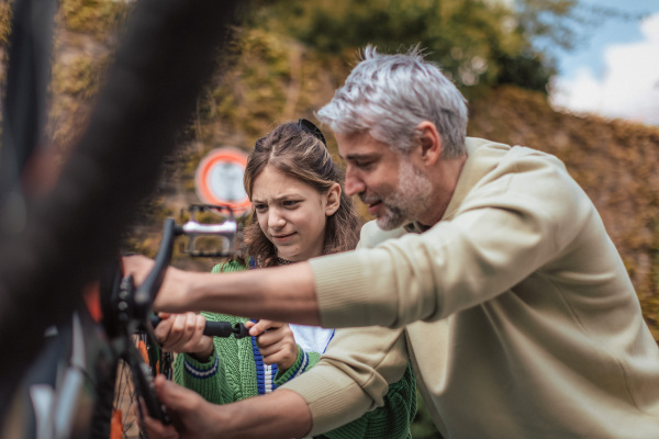 A happy father with teenage daughter repairing bicycle in street in town.