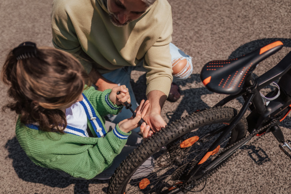 A happy father with teenage daughter repairing bicycle in street in town.