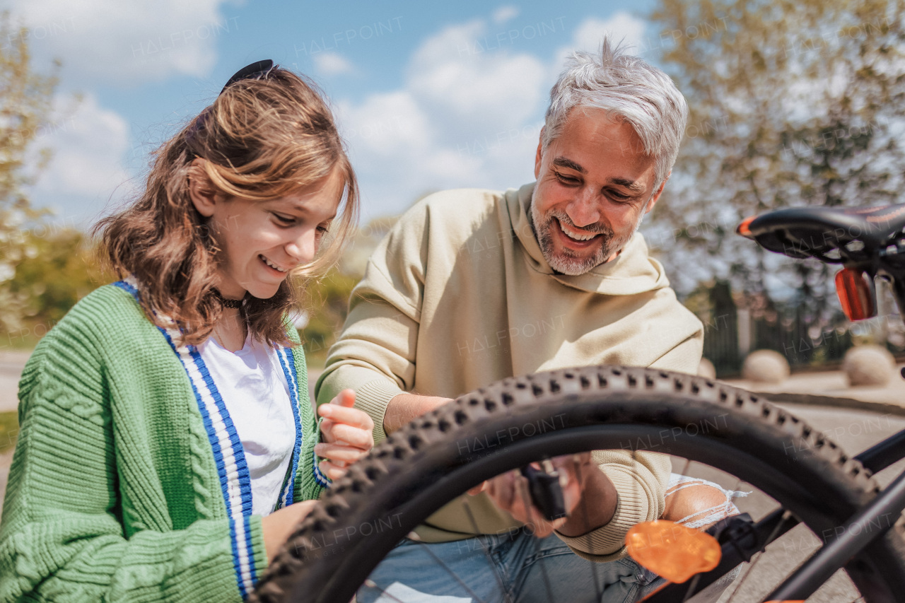 A happy father with teenage daughter repairing bicycle in street in town.