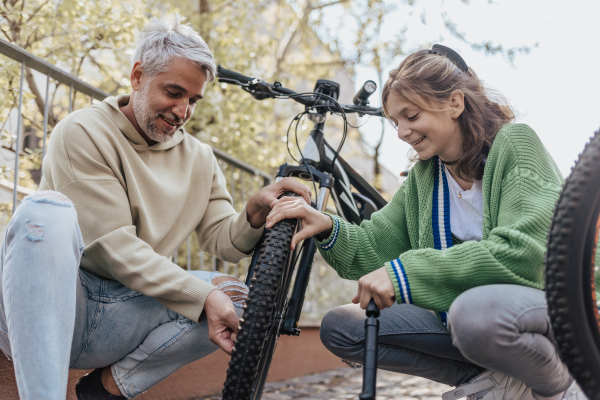 A happy father with teenage daughter repairing bicycle in street in town.