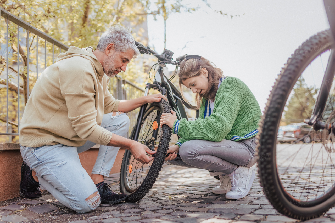 A happy father with teenage daughter repairing bicycle in street in town.