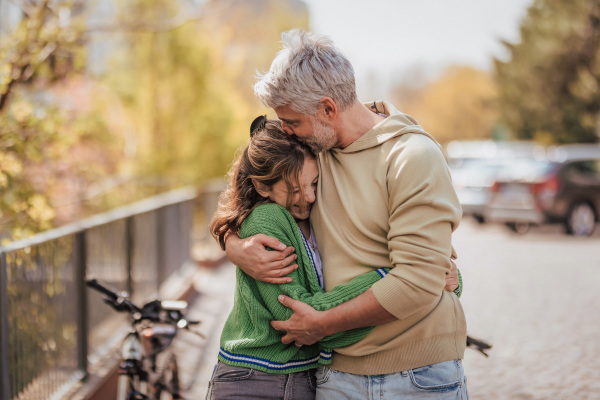 A teenage daughter hugging her father outside in town when spending time together.