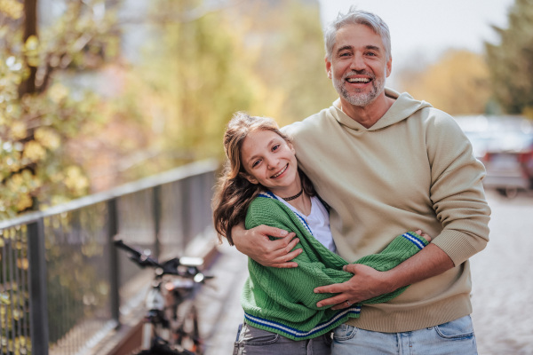 A teenage daughter hugging her father outside in town when spenidng time together.