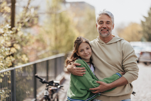 A teenage daughter hugging her father outside in town when spenidng time together.