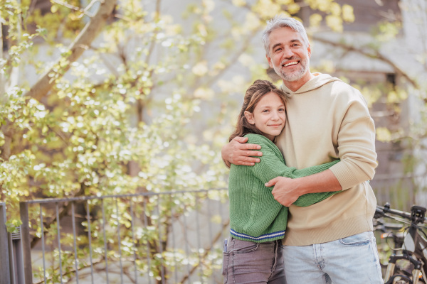 A teenage daughter hugging her father outside in town when spenidng time together.