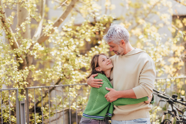 A teenage daughter hugging her father outside in town when spending time together.