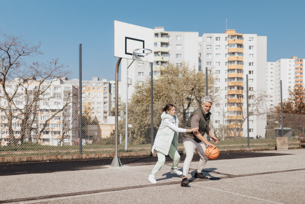 A happy father and teen daughter embracing and looking at camera outside at basketball court.