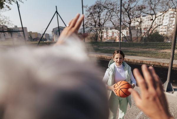 A happy father and teen daughter embracing and looking at camera outside at basketball court.