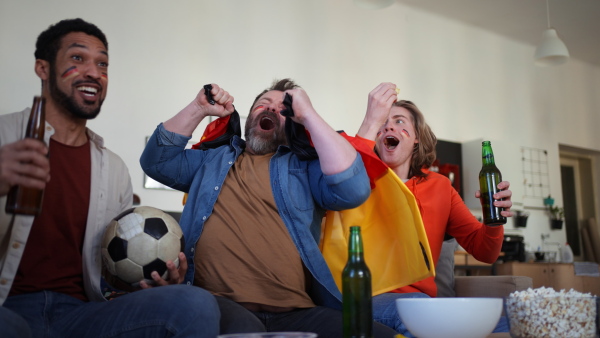 Happy German football fans friends watching a football at home and applauding