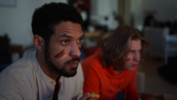 Nervous football fans friends staring at TV and watching football match at home.