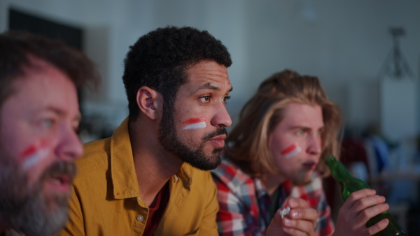 Nervous football fans friends staring at TV and watching football match at home.