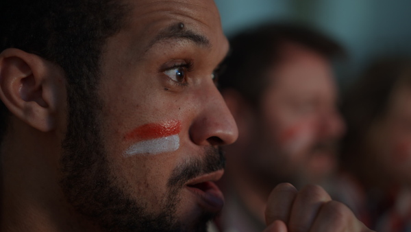 A close-up of excited football fan watching match with friends at home.