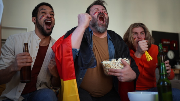 Happy German football fans friends watching a football at home and applauding