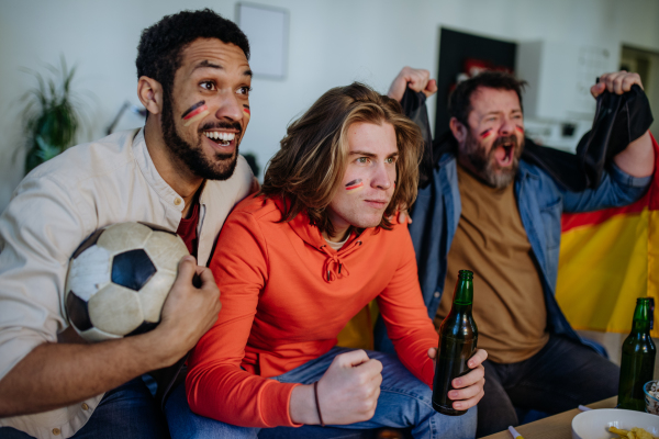 Happy German football fans friends watching football at home and celebrating success