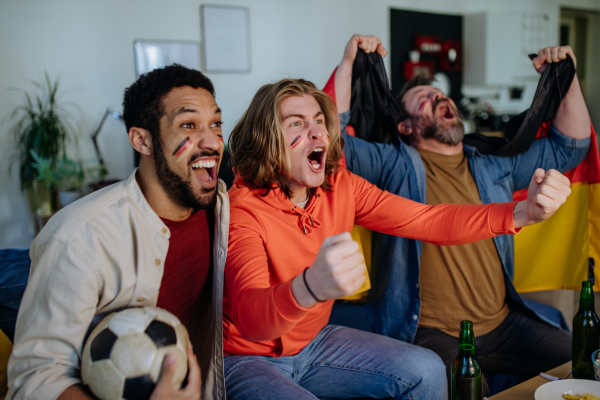 Happy German football fans friends watching football at home and celebrating success