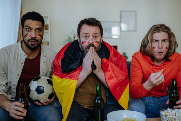 Nervous football fans friends staring at TV and watching football match at home.