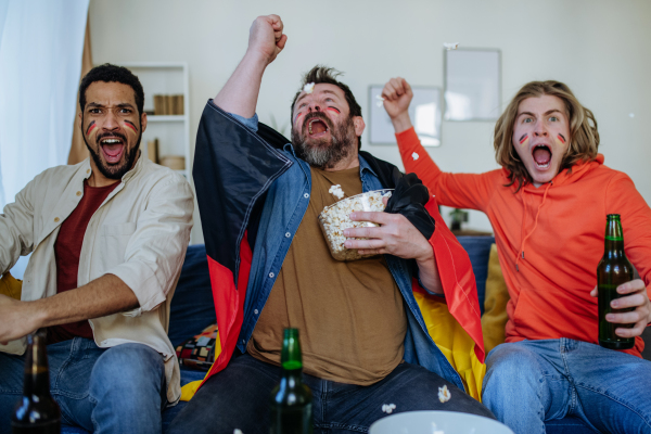 Happy German football fans friends watching football at home and celebrating success