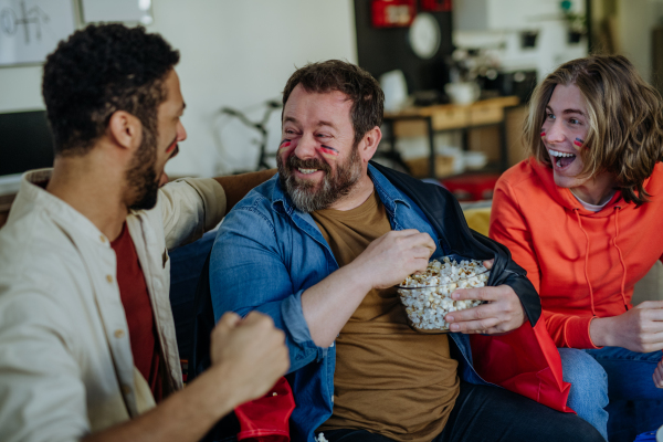 Happy German football fans friends watching football at home and eating the popcorn.