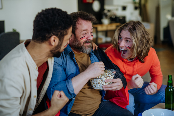 Happy German football fans friends watching football at home and eating the popcorn.