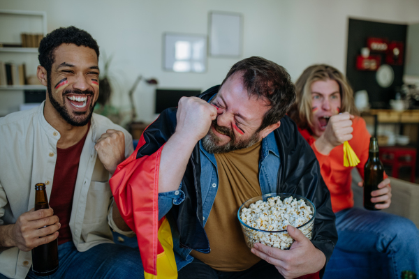 Happy German football fans friends watching football at home and eating the popcorn.