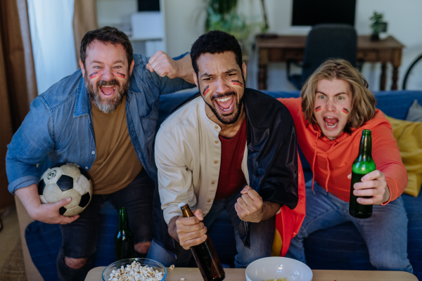 Happy German football fans friends watching football at home and eating the popcorn.