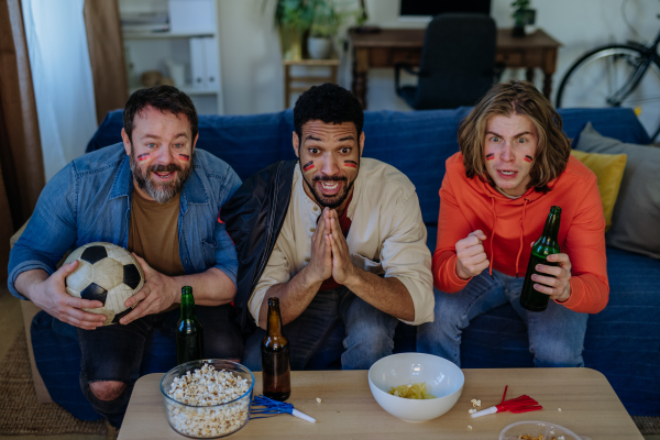 Nervous football fans friends staring at TV and watching football match at home.