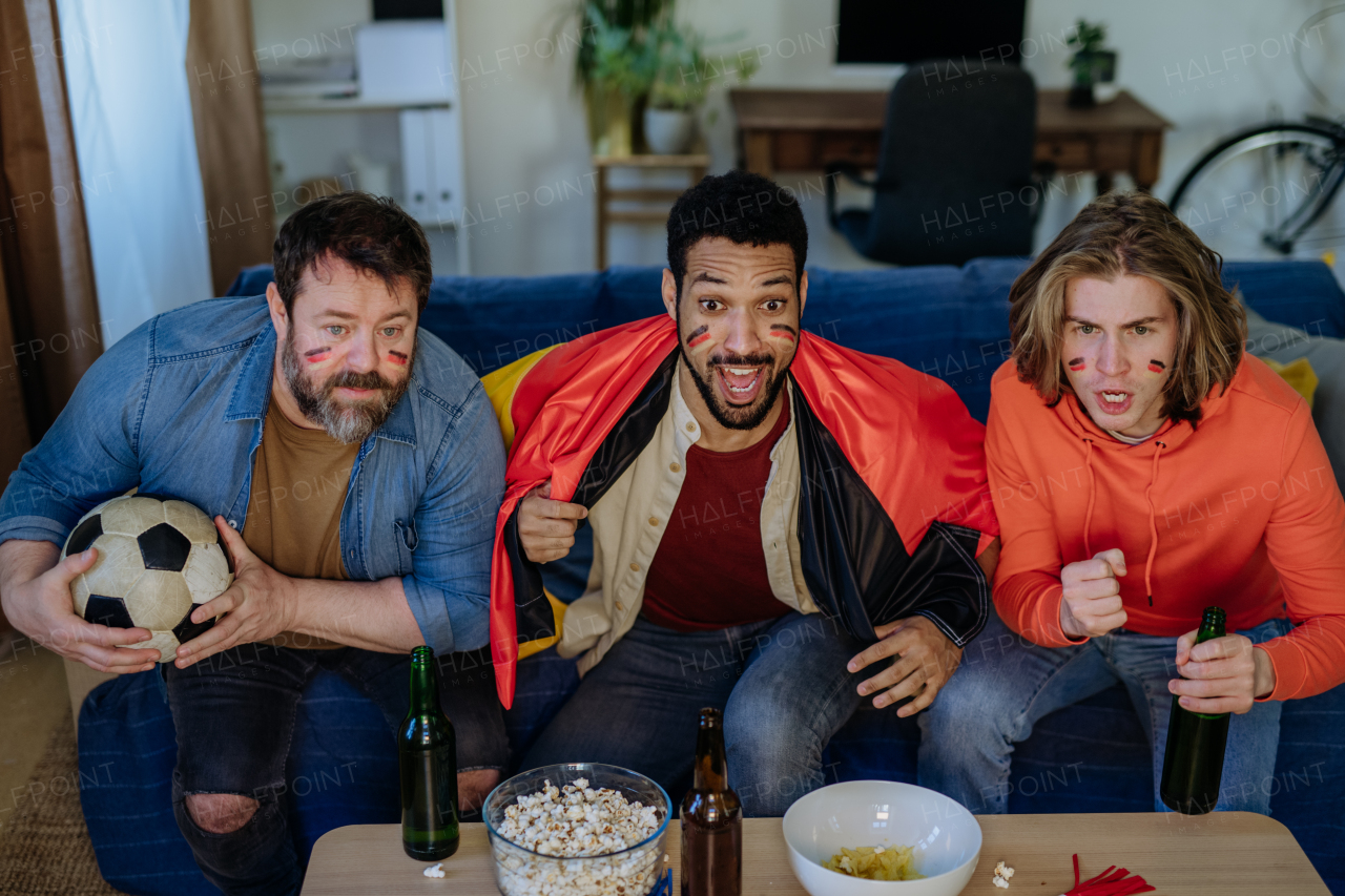 Nervous football fans friends staring at TV and watching football match at home.